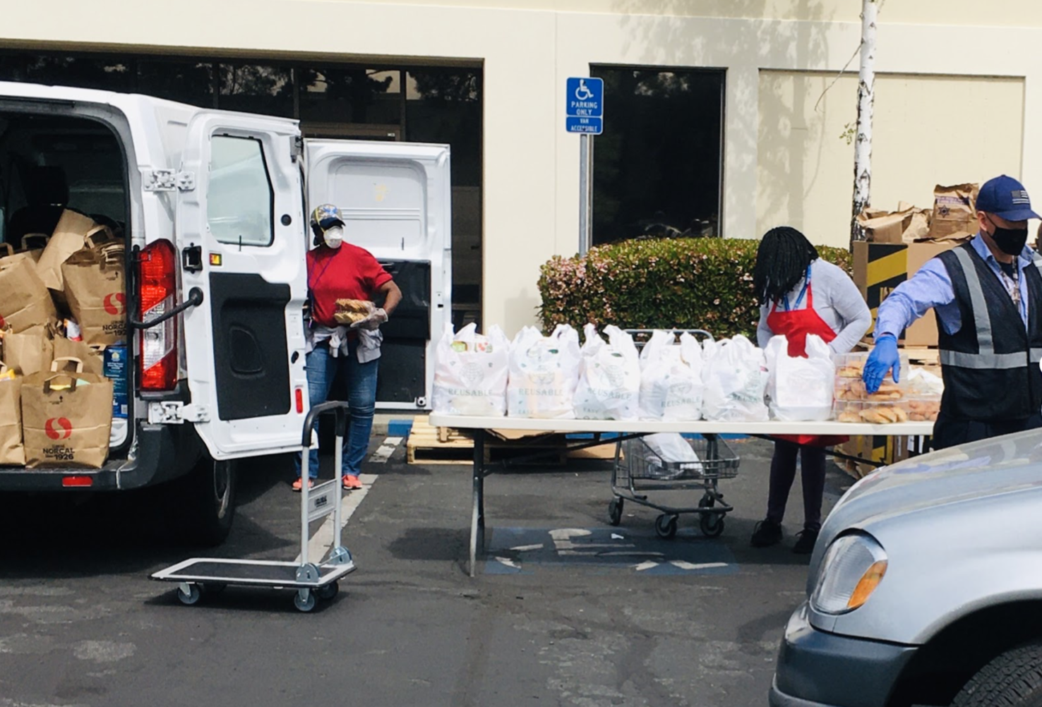 Plastic bags line a portable table in a parking lot, ready to be picked up via drive through at Arsola Food Pantry.