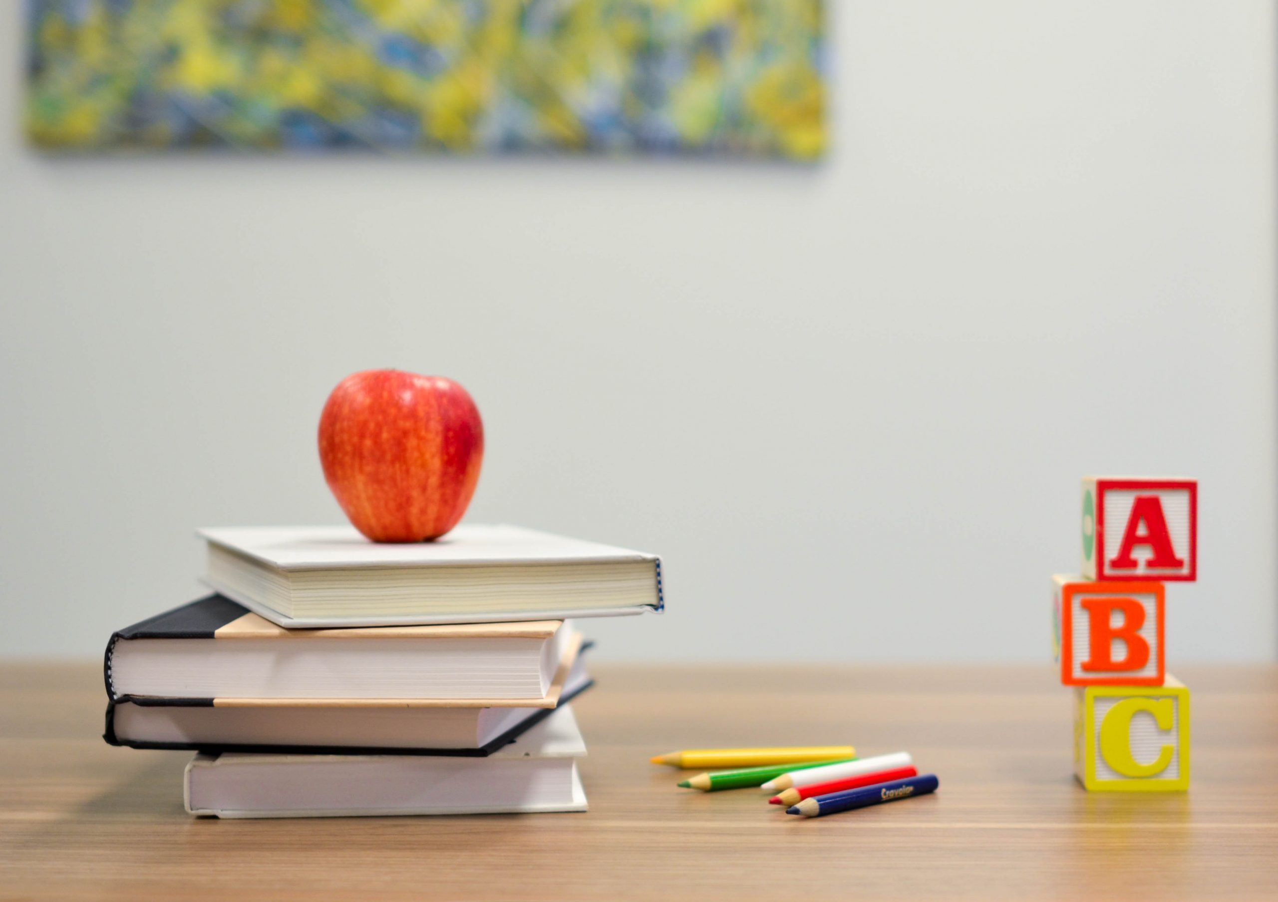 An image of a desk with a few books, an apple, and ABC blocks