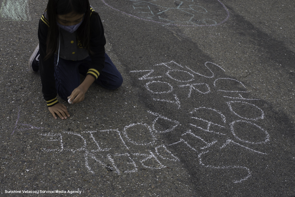 A child writes on the ground in chalk. It says "schools for children not police."