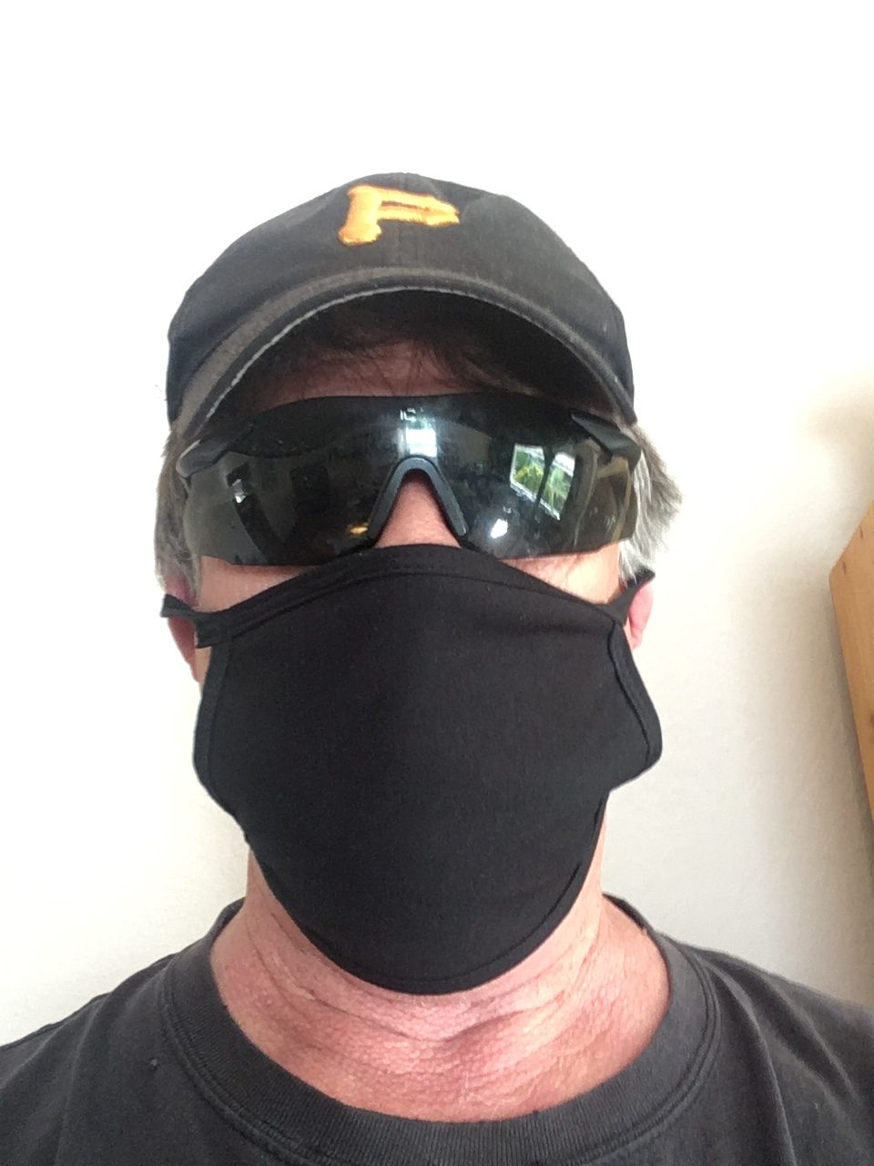 A man wears a cap, glasses, and a black mask