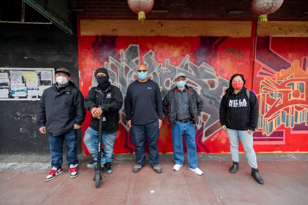 A diverse group of Asian Americans stand in front of a bright mural in Chinatown