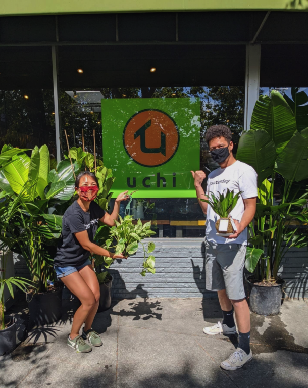 A Japanese American woman and African American/Filipino plan stand in front of a storefront that says "Uchi Time" with masks and smiles
