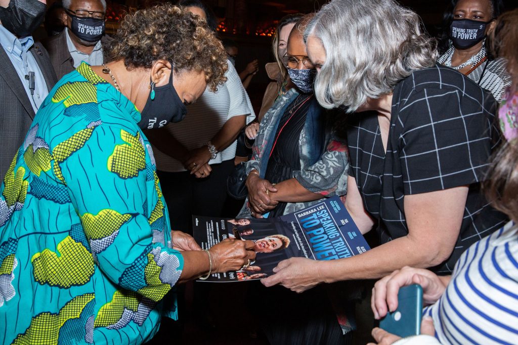 An African American woman with short hair and bright turquoise shirt signs a movie poster.