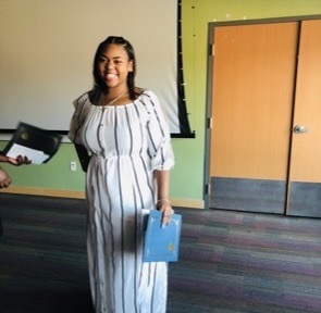 A smiling young African American woman wearing an off shoulder long white dress