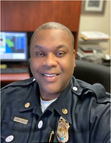 A bald African American man wearing a firefighter uniform sits in office