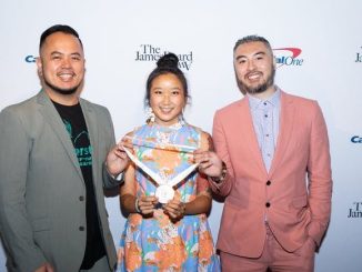 A Filipino American man, Chinese American woman, and Chinese American man dressed in festive outfits stand in front of backdrop that says "James Beard"
