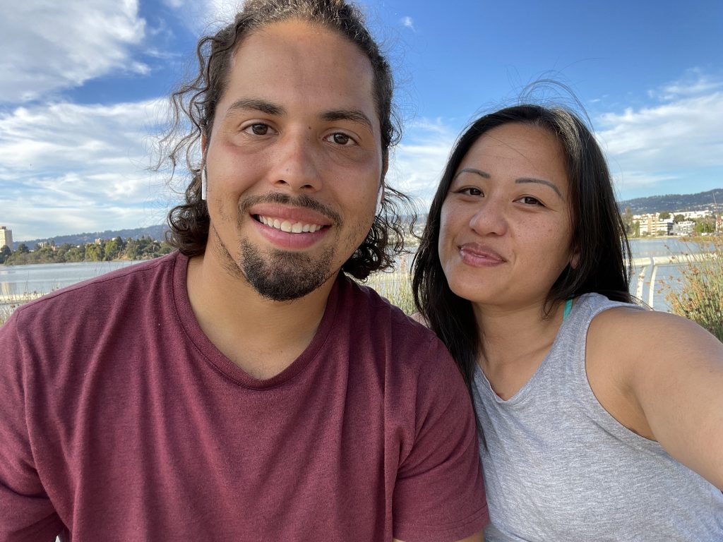 picture of man in light maroon shirt next to woman in grey tank top in front of Lake