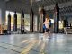 A boxing gym in East Oakland with concrete floors and bags handing from ceiling while one man is boxing in the right corner