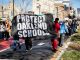 protesters walk with large black and white banner that says "protect Oakland schools"