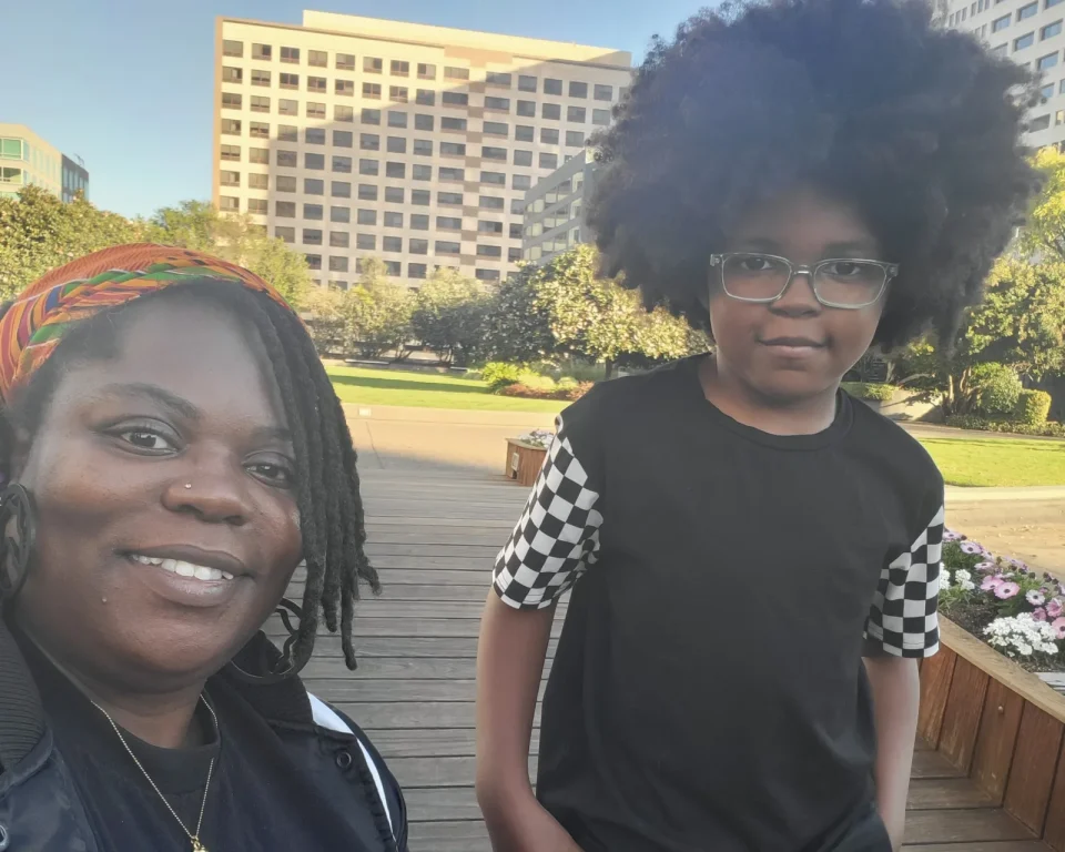An African American woman smiles into camera next to a young African American boy wearing glasses