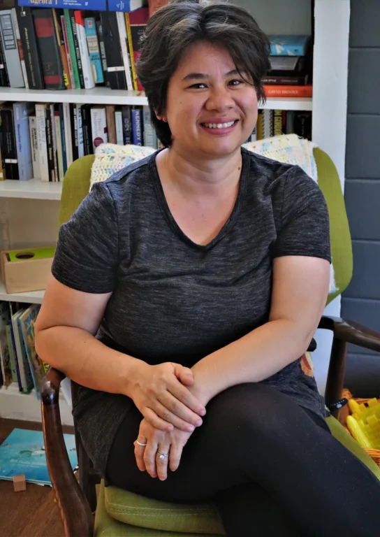 Asian American woman with short pixie cut sits in yellow chair for portrait