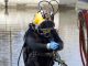 A man in a wetsuit and a yellow hard helmet comes out of murky waters