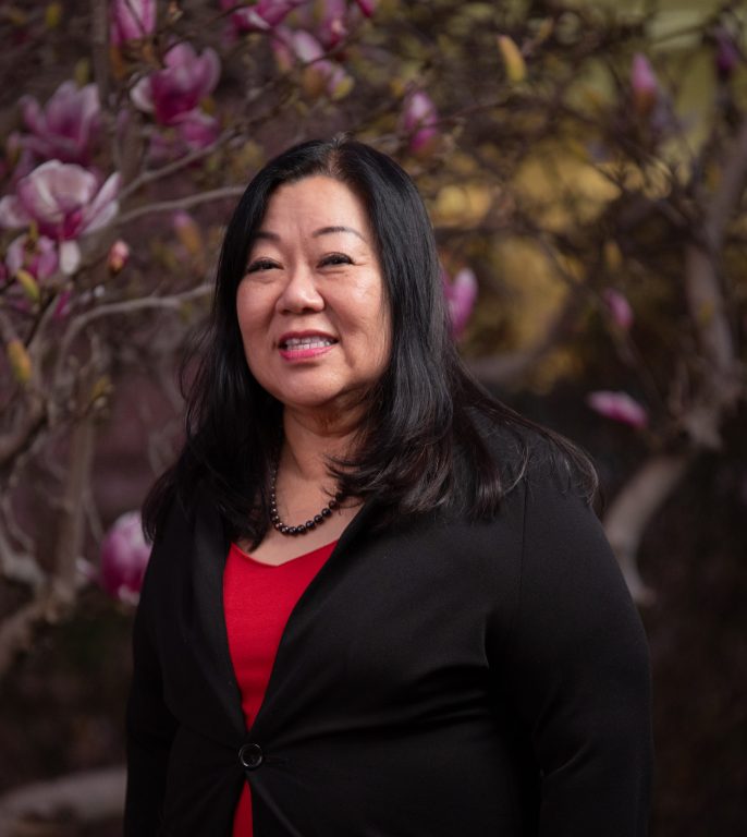 A Chinese American woman wearing black blazer and red shirt stands for portrait