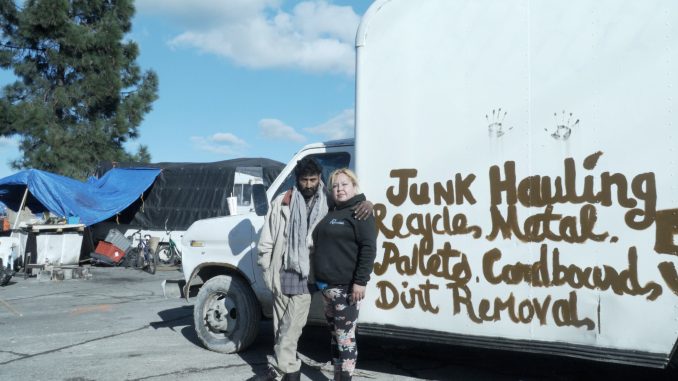 two people stand in front of a white truck that has hand lettering on it saying "junk hauling, metal..."