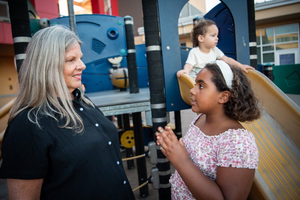 A white woman with silver straight hair talks with a young mixed race child