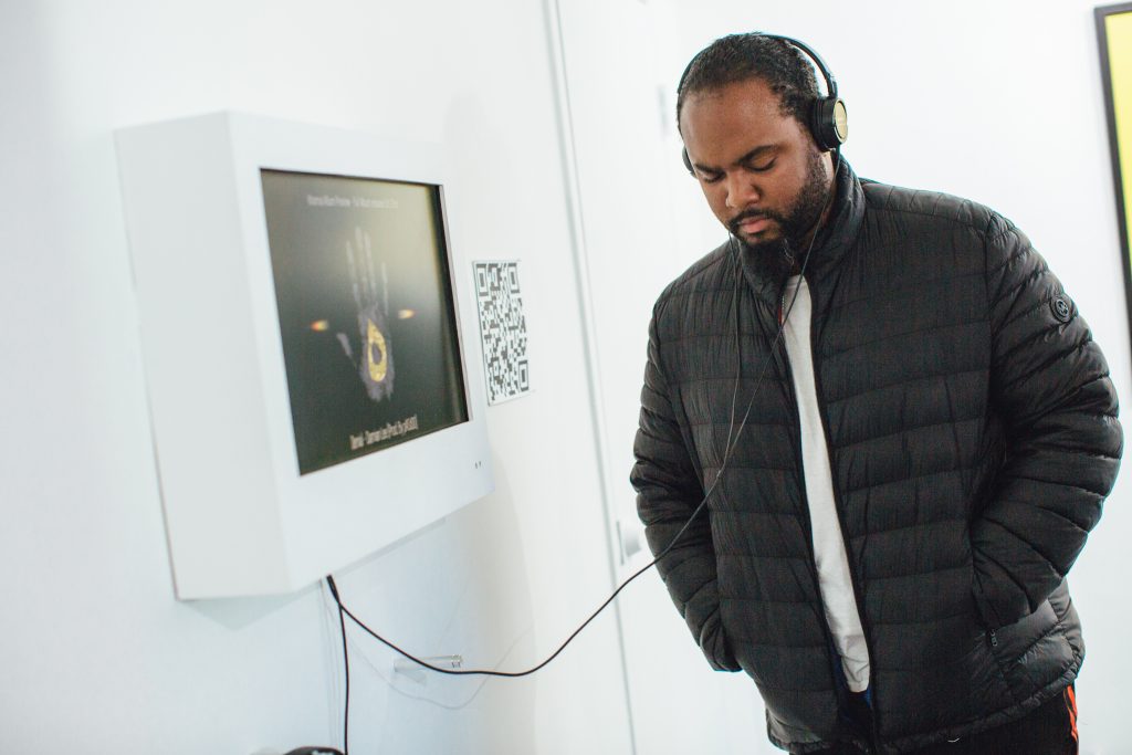 A Black man listens to a video that is part of an art installation