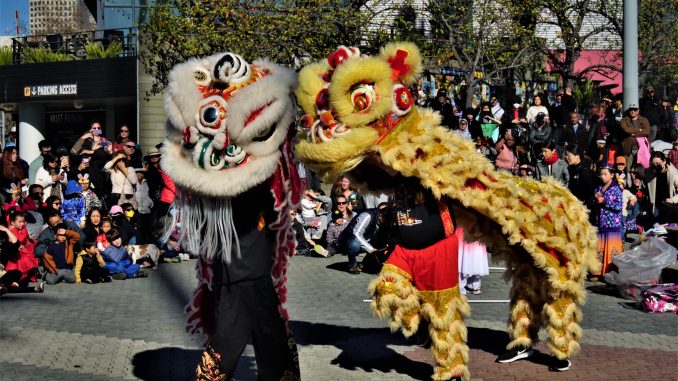 A black and a yellow lion dancer perform outside at Jack London Square