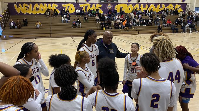 A group of basketball players surround a coach in an indoor game