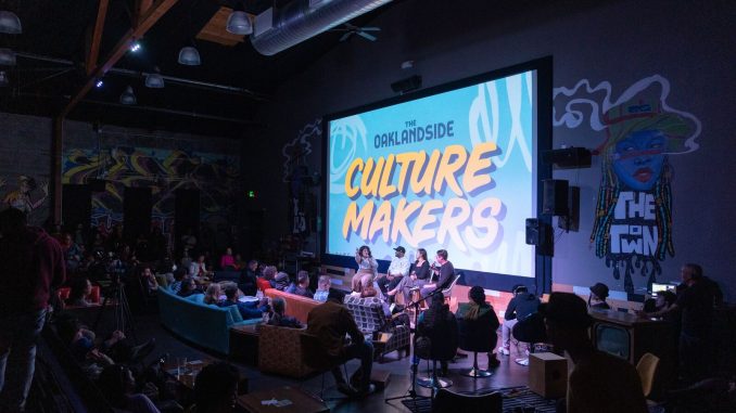 a dark theater with a screen that says "Oaklandside Culture Makers" and a panel in front