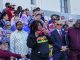 An African American woman with curly hair holding red sunglasses speaks into a mic in front of a courthouse