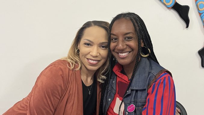Two African American women hug next to each other and smile for a photo