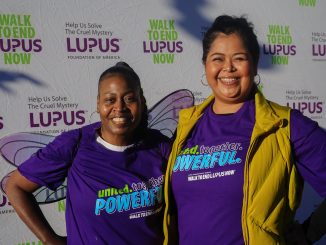 An African American woman and Latina woman stand next to each other during a charity walk wearing purple t-shirts