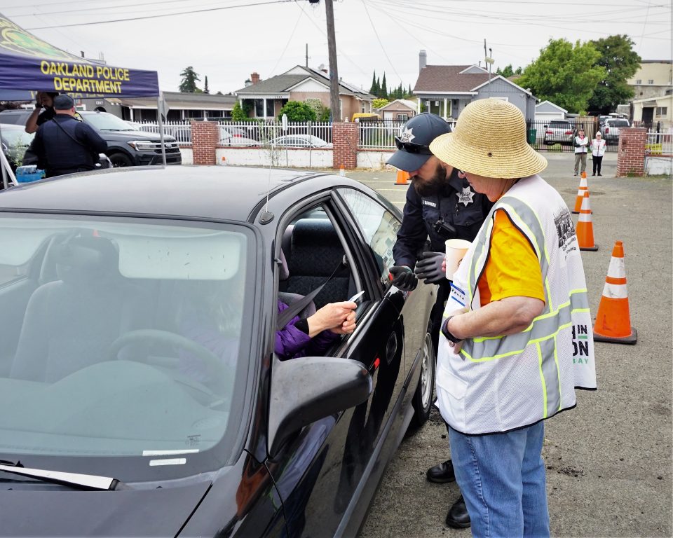 a woman wearing a straw hat talks to someone in a car with their windows down