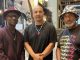 three Black men stand inside a large art exhibit and station in Oakland