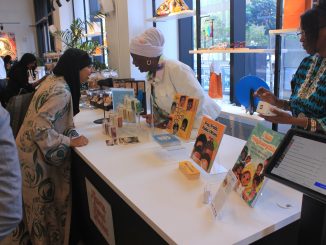 A woman wearing a head wrap shows another woman a book