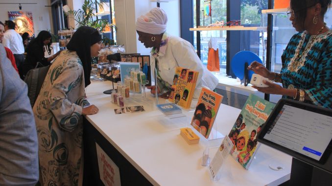 A woman wearing a head wrap shows another woman a book