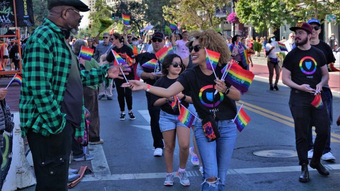 a Black woman passes out a rainbow flag to a Black elder man