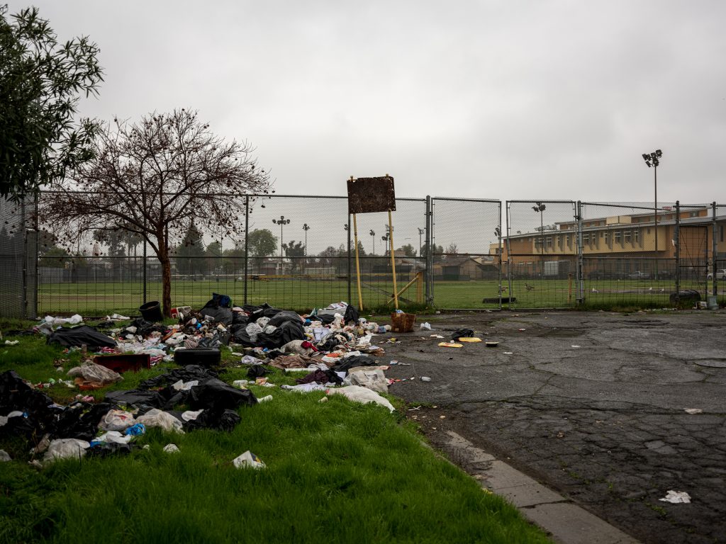 a pile of trash strewn across a green grassy field next to a fenced in school