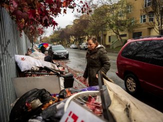 A woman on a sidewalk looks at a huge pile of dumped furniture on the sidewalk