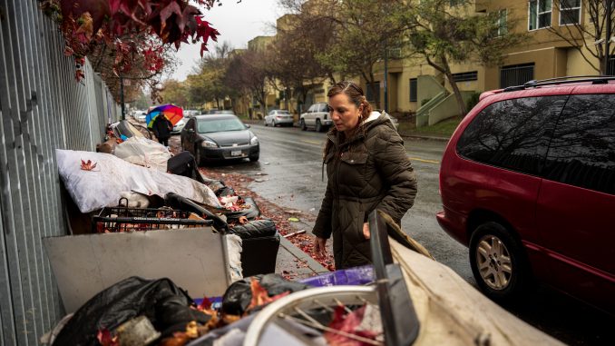 A woman on a sidewalk looks at a huge pile of dumped furniture on the sidewalk