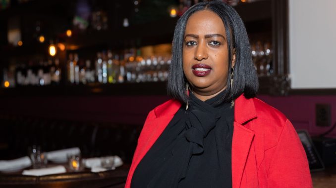 An African American woman with short straight hair wearing a red jacket poses for photo inside her restaurant