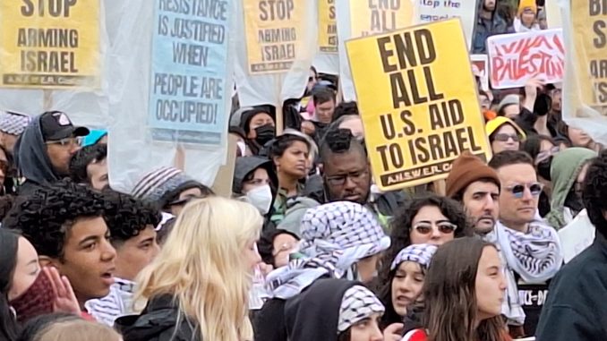 a diverse group of people holding protest signs about Israel's attack on Gaza