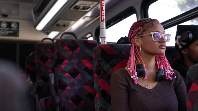 An African American girl sits inside a bus looking outside the window