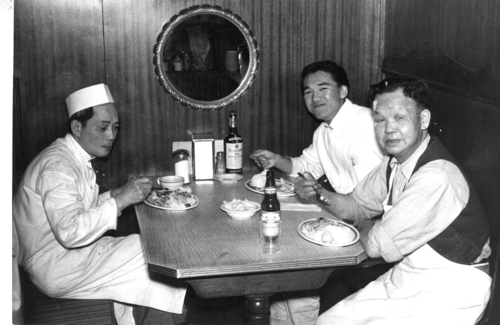 black and white photo of three Chinese American men eating inside a Chinese restaurant