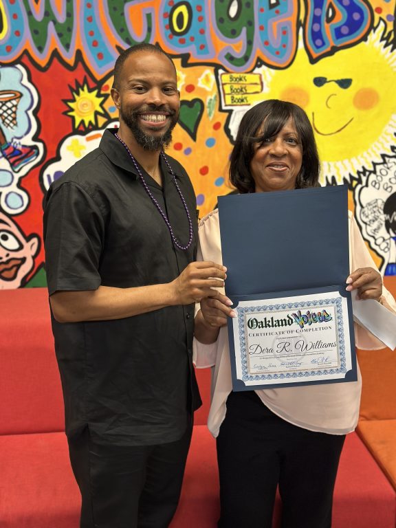 An African American man holds up a diploma with an African American woman.