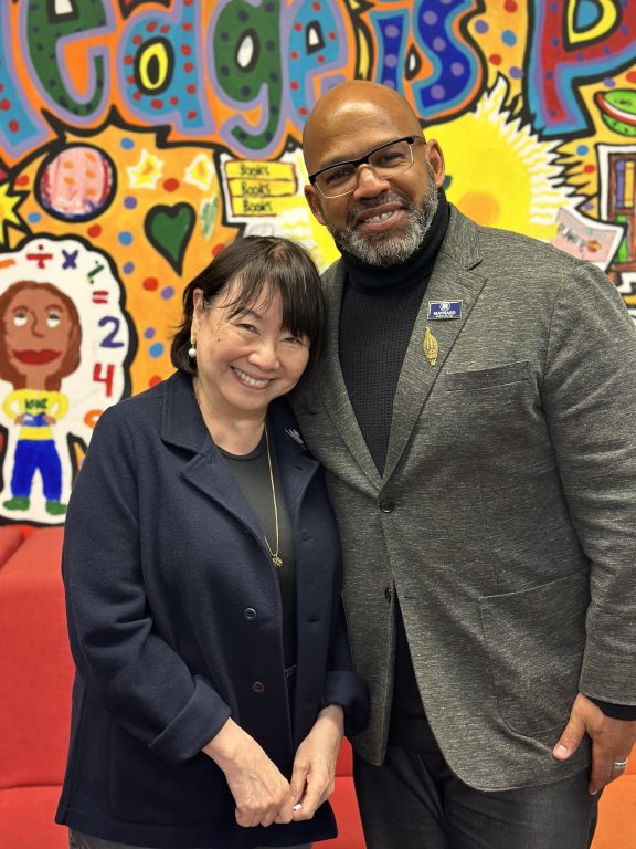 A Chinese American woman with an African American man pose together in front of a colorful mural inside the library