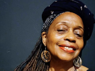 A Black woman wearing a black hat smiles at camera