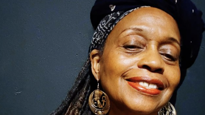 A Black woman wearing a black hat smiles at camera