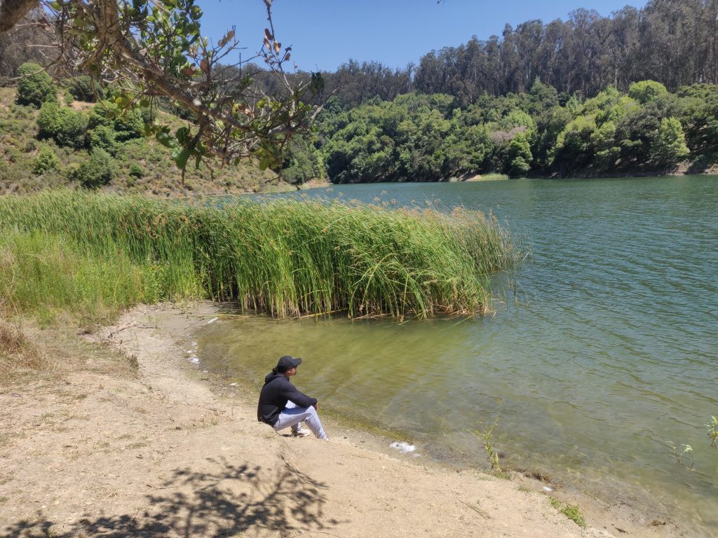 A man sits near an emerald colored lake