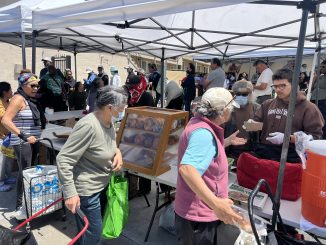 Groups of people gathering to receive food at the Sliding Scale Cafe.