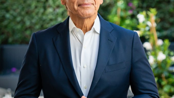 light brown latino mam wearing navy blue suit with open collar suit with slight smile and hands lightly held together