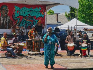 A woman speaks in front of drummers during Baba Mosheh’s Bantaba ensemble performance at the Malcolm X JazzArts Festival.