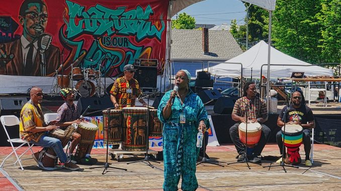 A woman speaks in front of drummers during Baba Mosheh’s Bantaba ensemble performance at the Malcolm X JazzArts Festival.